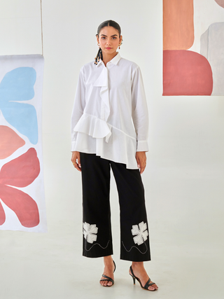 White asymmetric shirt paired with black pants with floral patch detail
