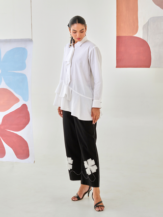 White asymmetric shirt paired with black pants with floral patch detail